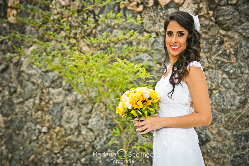 Foto da noiva segurando bouquet amarelo e branco com fundo de pedra em fotografia de Mariana Seelinger Fotógrafa de Casamentos em Niterói e RJ