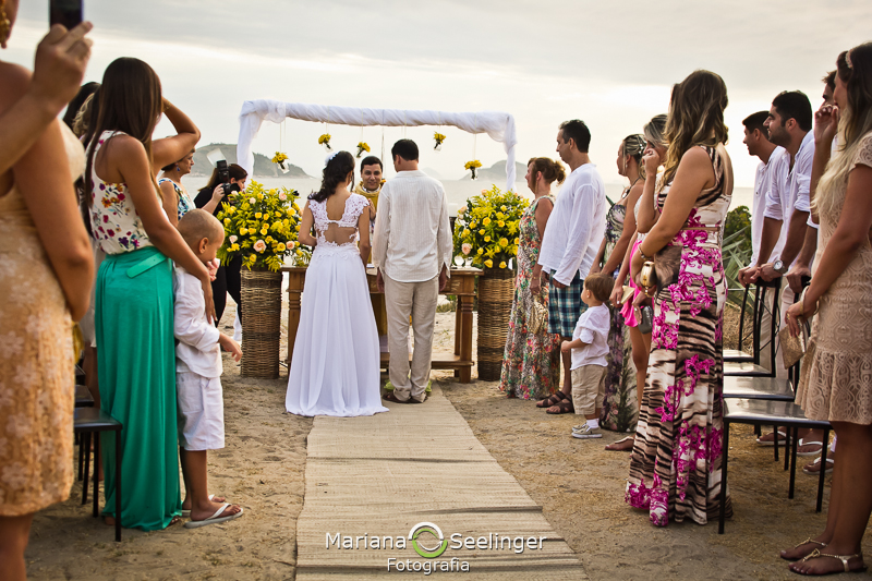 Noivos no altar decorado de flores amarelas na praia de camboinhas em fotografia de Mariana Seelinger Fotógrafa de Casamentos em Niterói e RJ