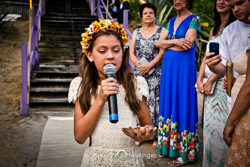 Daminha com coroa na cabeça cantando e levando as alianças para o casal de noivo em fotografia de Mariana Seelinger Fotógrafa de Casamentos em Niterói e RJ