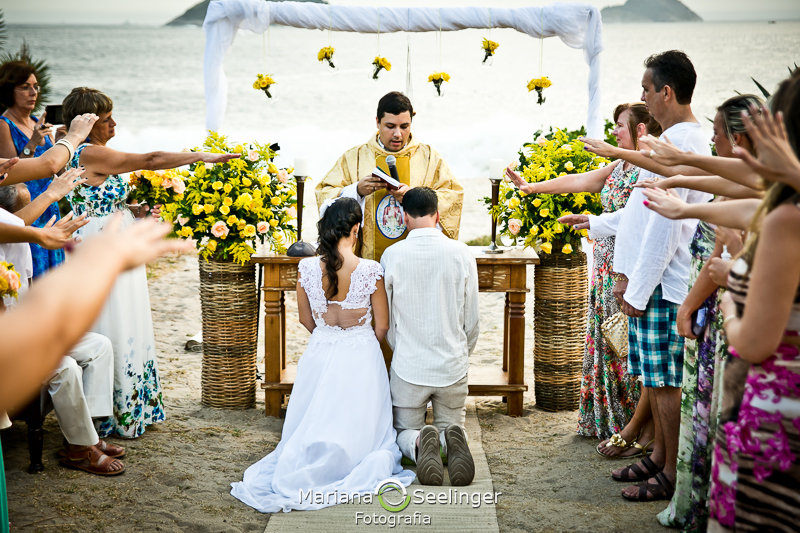 Noivos ajoelhados recebendo a benção do celebrante em fotografia de Mariana Seelinger Fotógrafa de Casamentos em Niterói e RJ