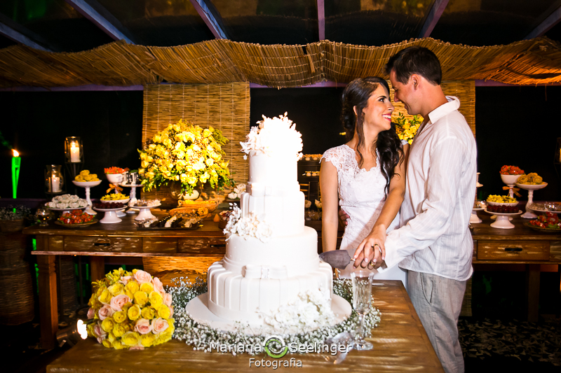 Bolo de 4 andares apoiado em mesa de madeira rústica em fotografia de Mariana Seelinger Fotógrafa de Casamentos em Niterói e RJ