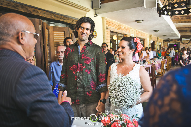 Noivos felizes escutando a celebração de seu casamento em fotografia de Mariana Seelinger Fotógrafa de Casamentos em Niterói e RJ