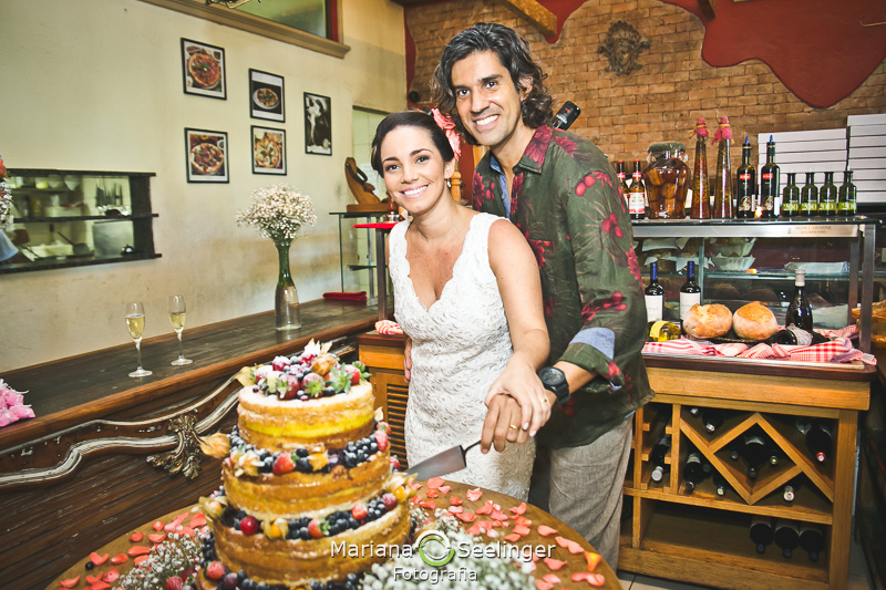 Noiva e noivo cortando o o bolo de casamento de três andares em fotografia de Mariana Seelinger Fotógrafa de Casamentos em Niterói e RJ