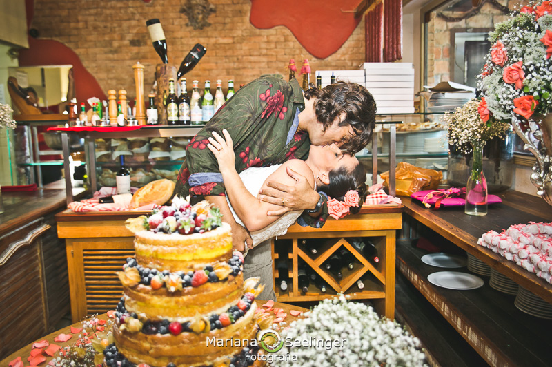 Noivos se beijando e no fundo a decoração italiana em fotografia de Mariana Seelinger Fotógrafa de Casamentos em Niterói e RJ