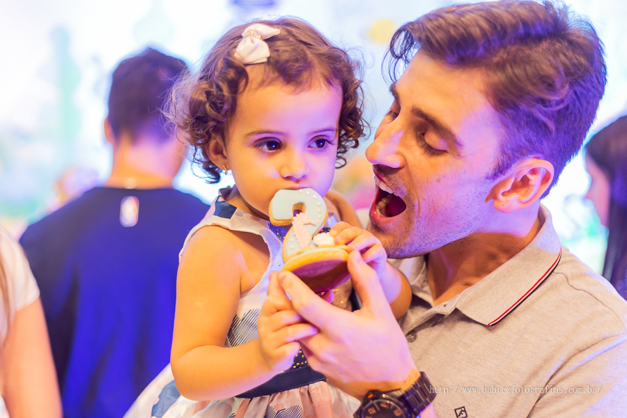 Fotografia da aniversariante comedo doces no colo do papai