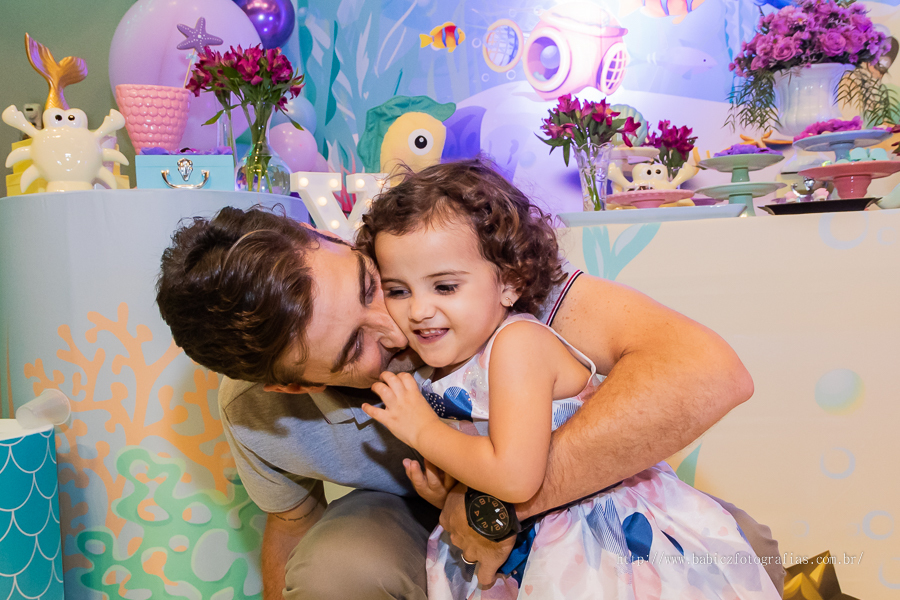 Fotografia da aniversariante comedo doces no colo do papai