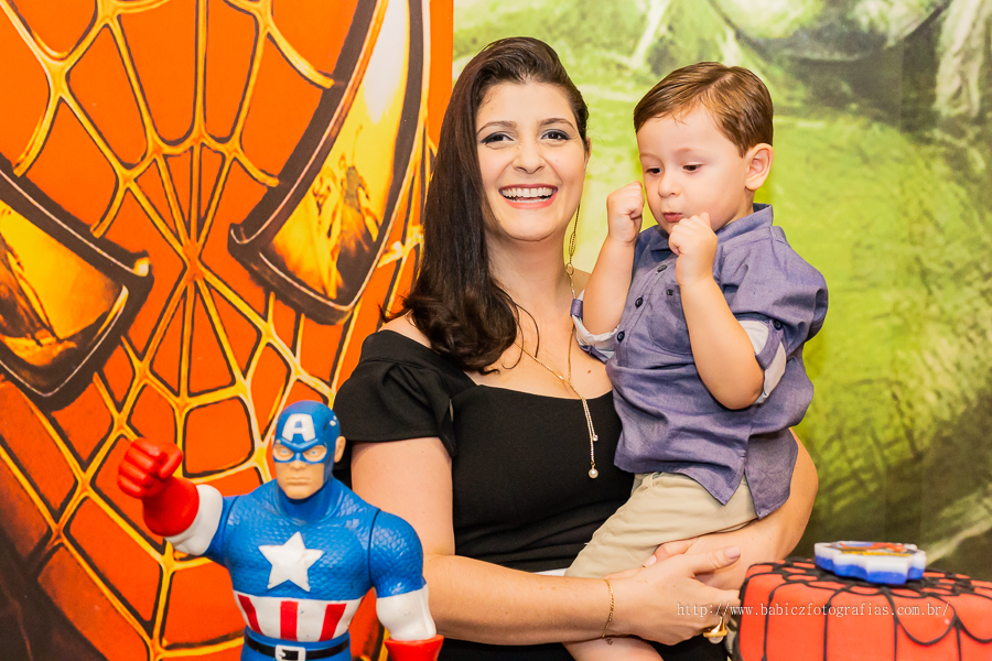 Fotografia do aniversariante Theo no cola da mamãe na mesa do bolo, com decoração da liga da justiça e vingadores no Jungle Frends em Maringá.