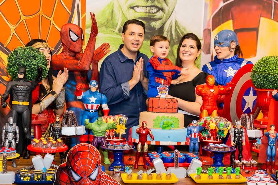 Foto do aniversariante Théo com os pais na mesa do bolo cantando parabens com os personagens da liga da justiça e vingadores no Jungle Frends em Maringá.