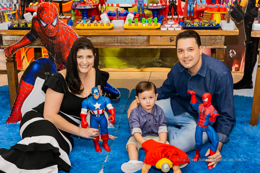 Fotografia do aniversariante Theo com os pais na mesa do bolo, com decoração da liga da justiça e vingadores no Jungle Frends em Maringá.