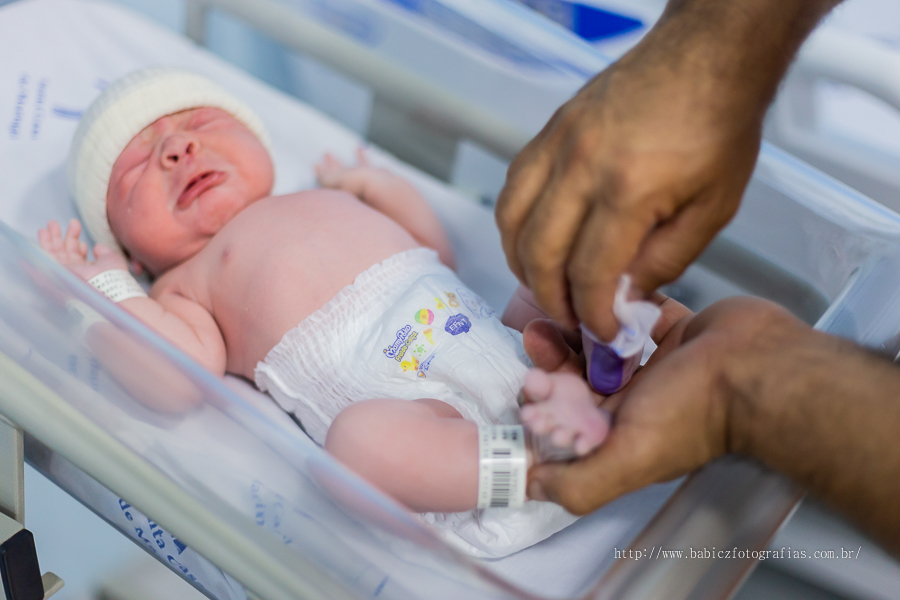 Fotografia do nascimento parto do Samuel na Maternidade Santa Casa Maringá. Pela fotografa Rose Babicz. Apos o nascimento podemos ver o bebe com tinta azul no pezinho e as mãos do papai limpando.