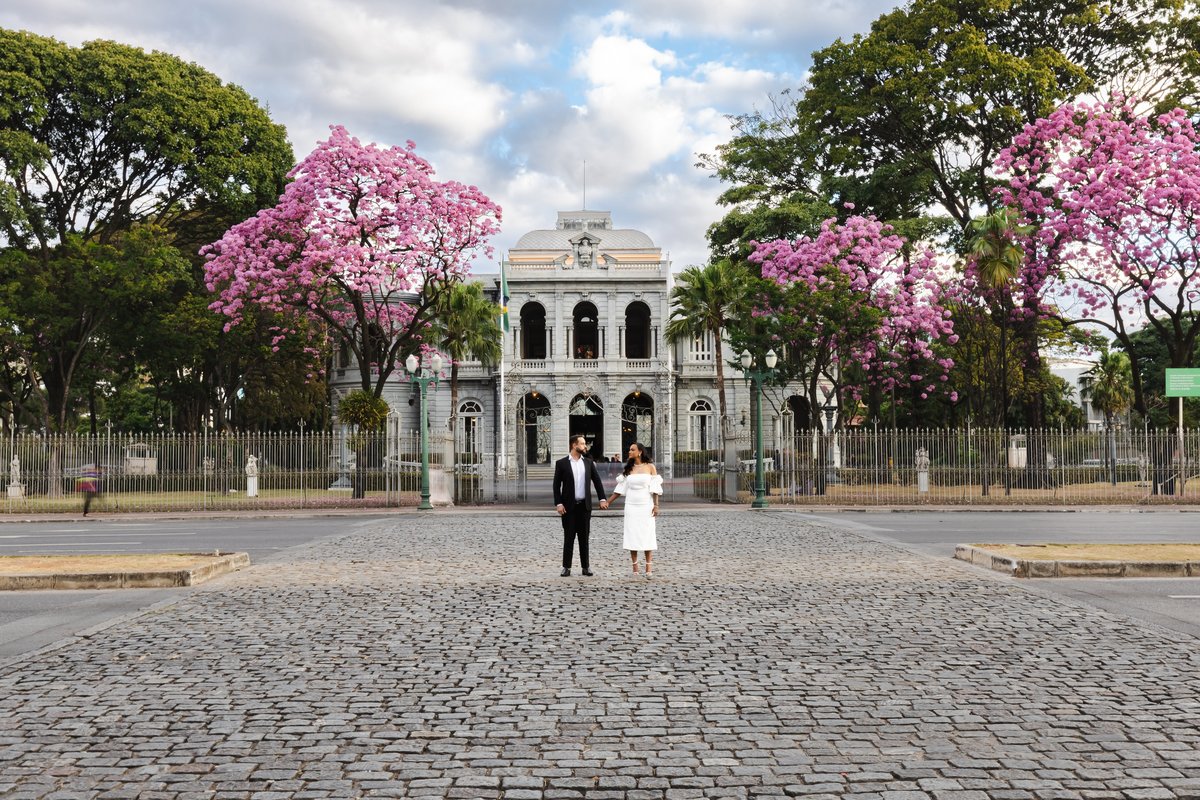 Casal em frente ao Palácio da Liberdade cercado pelos ipês floridos 