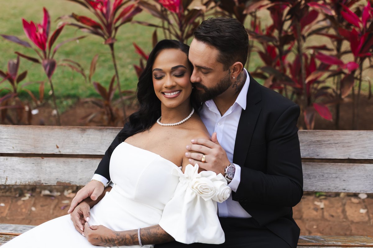Nathalia e Enrico abraçados entre as flores vermelhas da praça