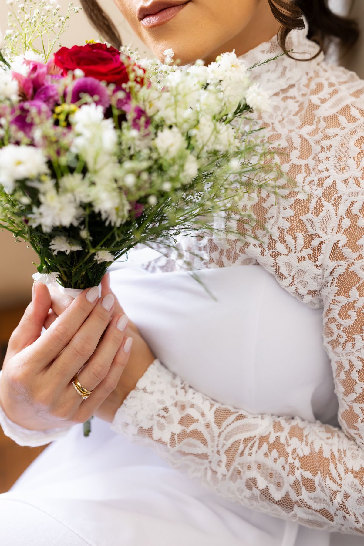 Detalhe das mãos da noiva com anel de noivado e buquê de flores