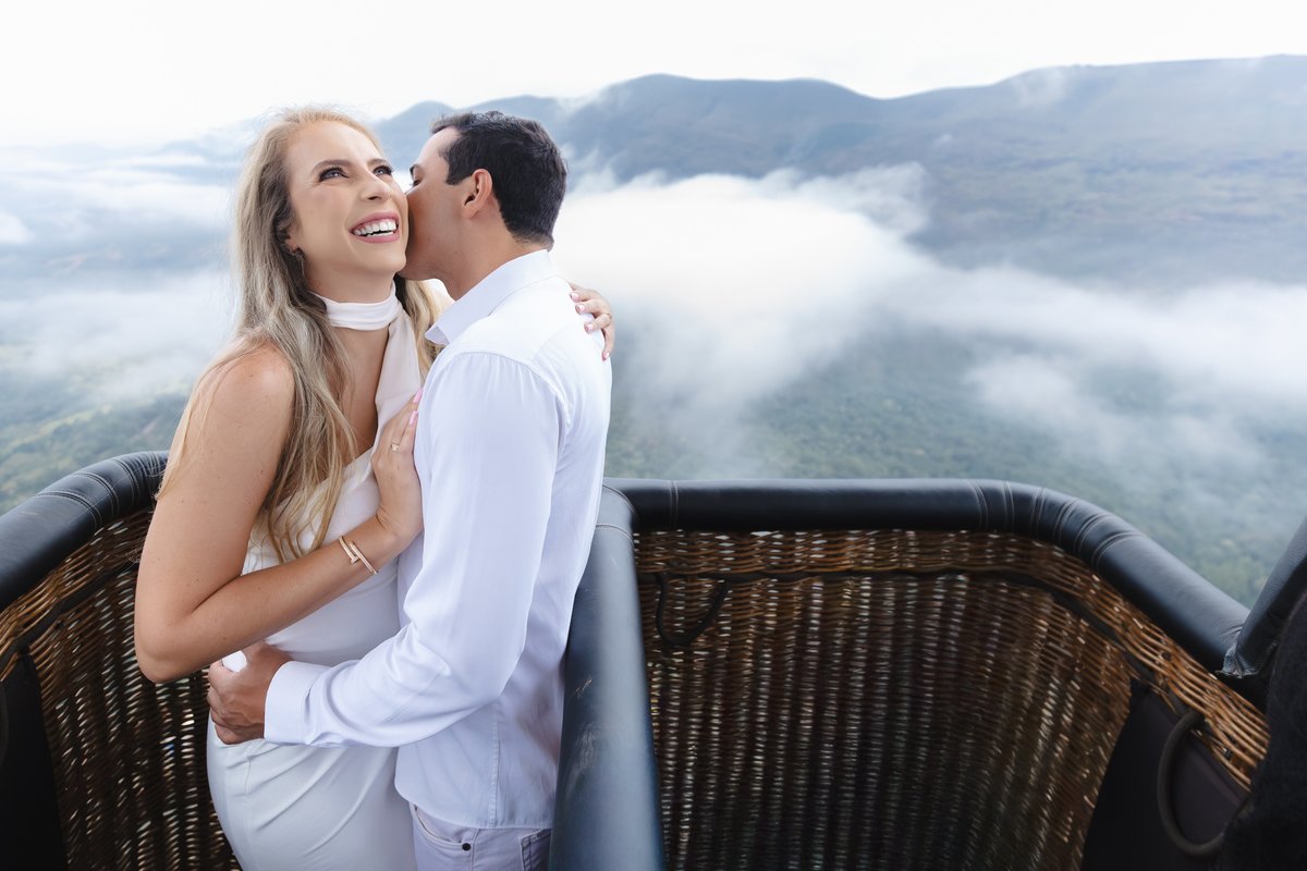 Foto de casal no cesto do balão com nuvens e montanhas ao fundo