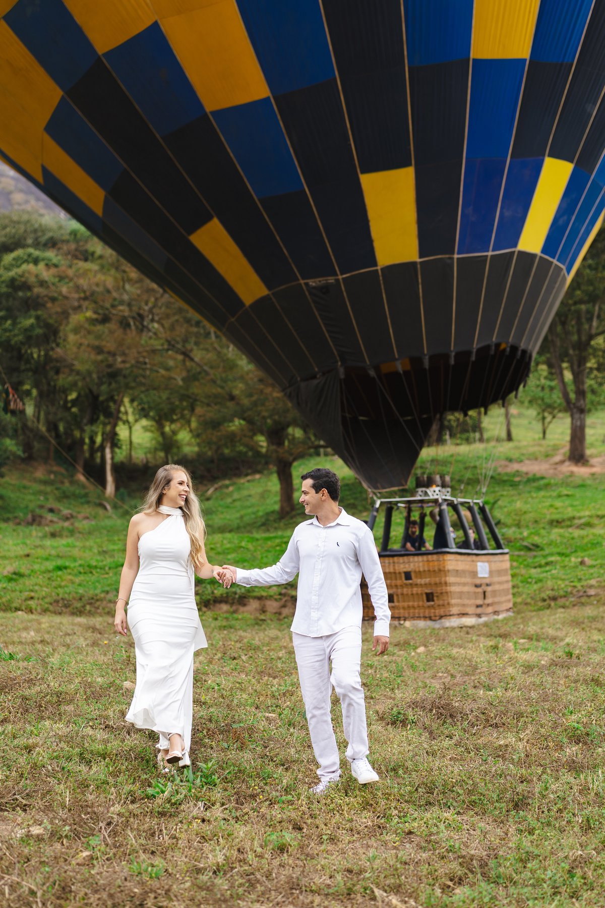 Noivos caminhando de mãos dadas no campo com balão ao fundo