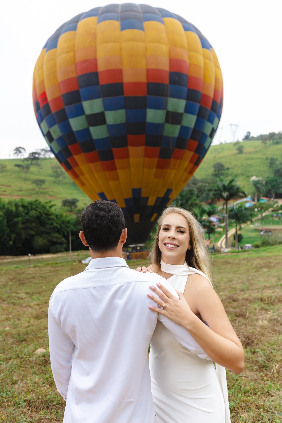 Noiva olhando para a câmera com noivo de costas e balão colorido ao fundo