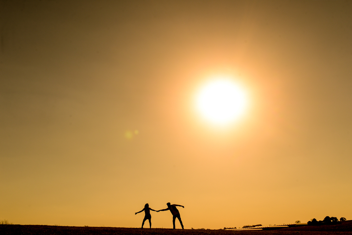 ensaio do casal pre-wedding noiva puxando noivo com o sol de fundo somente silhueta do casal foto minimalista  feita em Holambra cidade das flores 