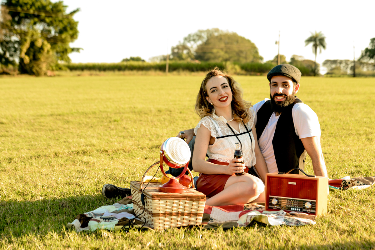 ensaio retro casal com estilo unico com coisas antigas no cenário como radio antigo garrafa de coca-cola com um gramado verde feito na plantação de feno em Holambra cidade das flores 