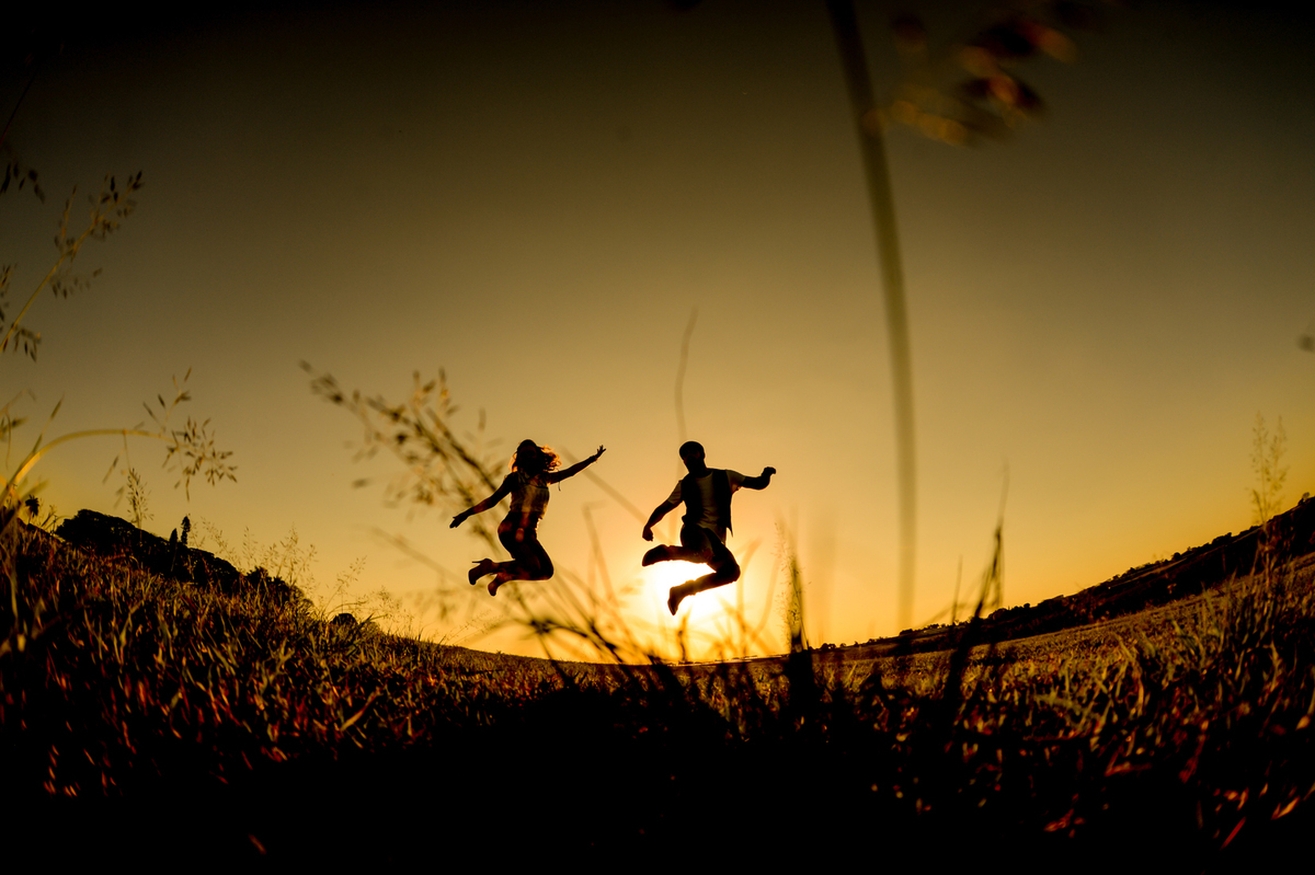 casal juntos pulando com uma silhueta  no ensaio de pre-wedding em uma plantação de trigo feita no por do sol em Holambra cidade das flores 