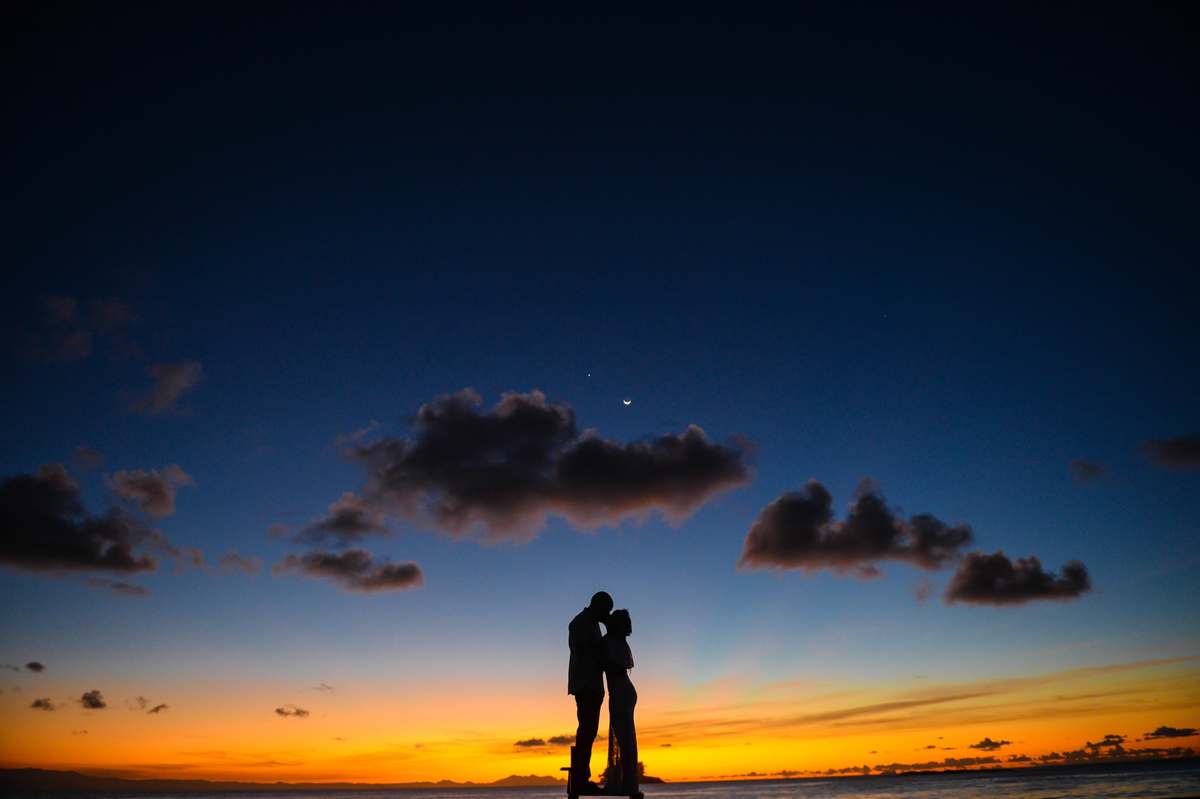 foto do casal somente silueta  em cima de uma escada de frente um para o outro  bem juntos com o sol nascendo  no mar ao fundo 