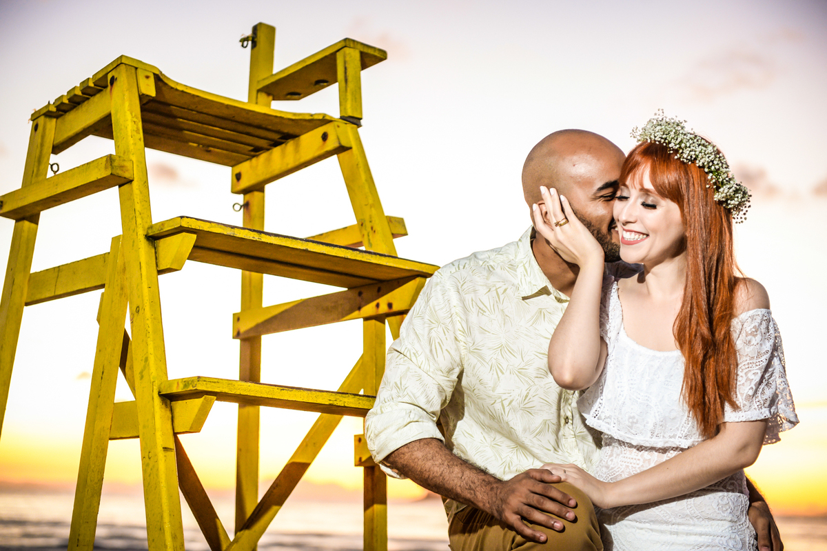 casal juntos sentado em uma escada de salva vidas com o nascer do sol na praia ao fundo 