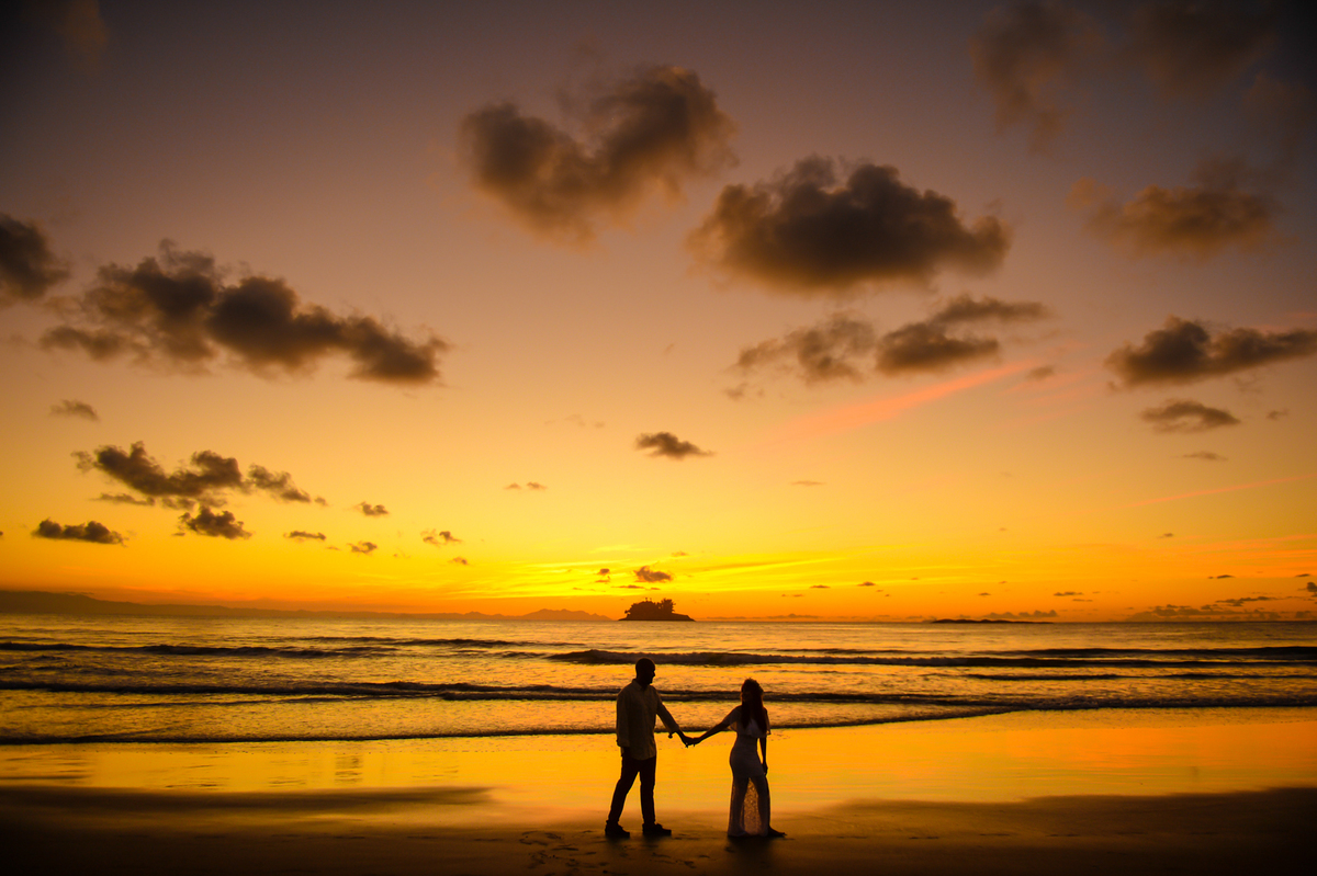 noiva puxando noivo na praia com o nascer do sol ao fundo 