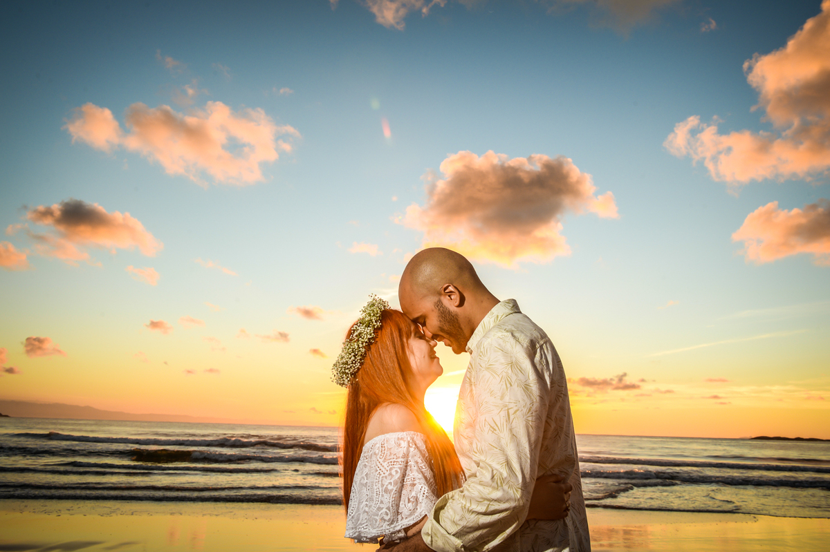 casal bem juntinho  um olhando para o outro com um olhar bem apaixonado bem romantico na praia com o sol nascendo ao fundo 