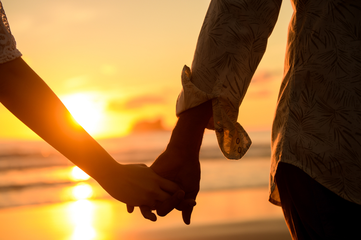 casal bem juntinho  um olhando para o outro com um olhar bem apaixonado bem romantico na praia com o sol nascendo ao fundo somente a silhueta do casal como sol no centro 