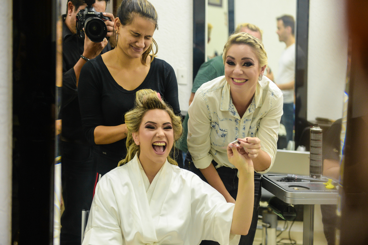 noiva toda sorridente na hora de fazer o cabelo com a amiga ao lado 