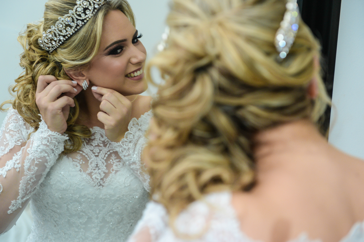noiva toda pronta ja maquiada com a cabelo penteado e coroa na cabeca colocando brinco de cristal 