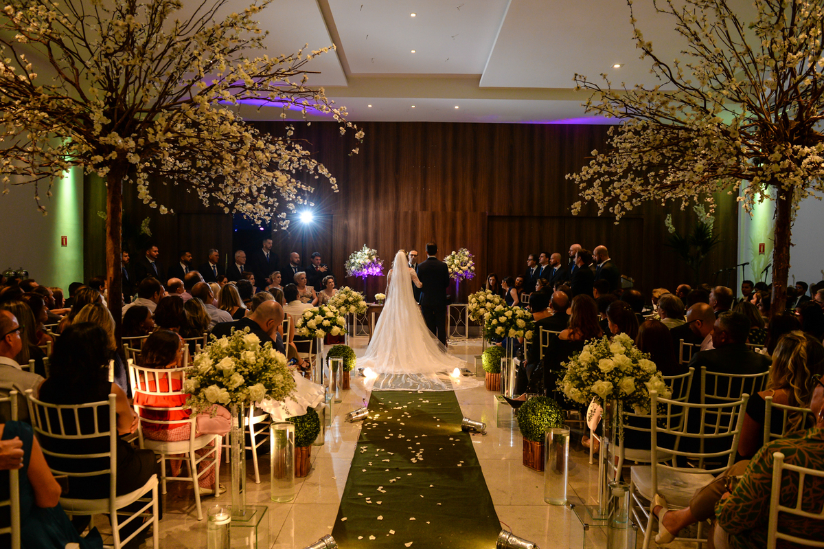 foto feita la do fundo pegando o vestido da noiva toda aberto e mostrando  o corredor com o tapete verde e as arvores que ajudava na decoração 