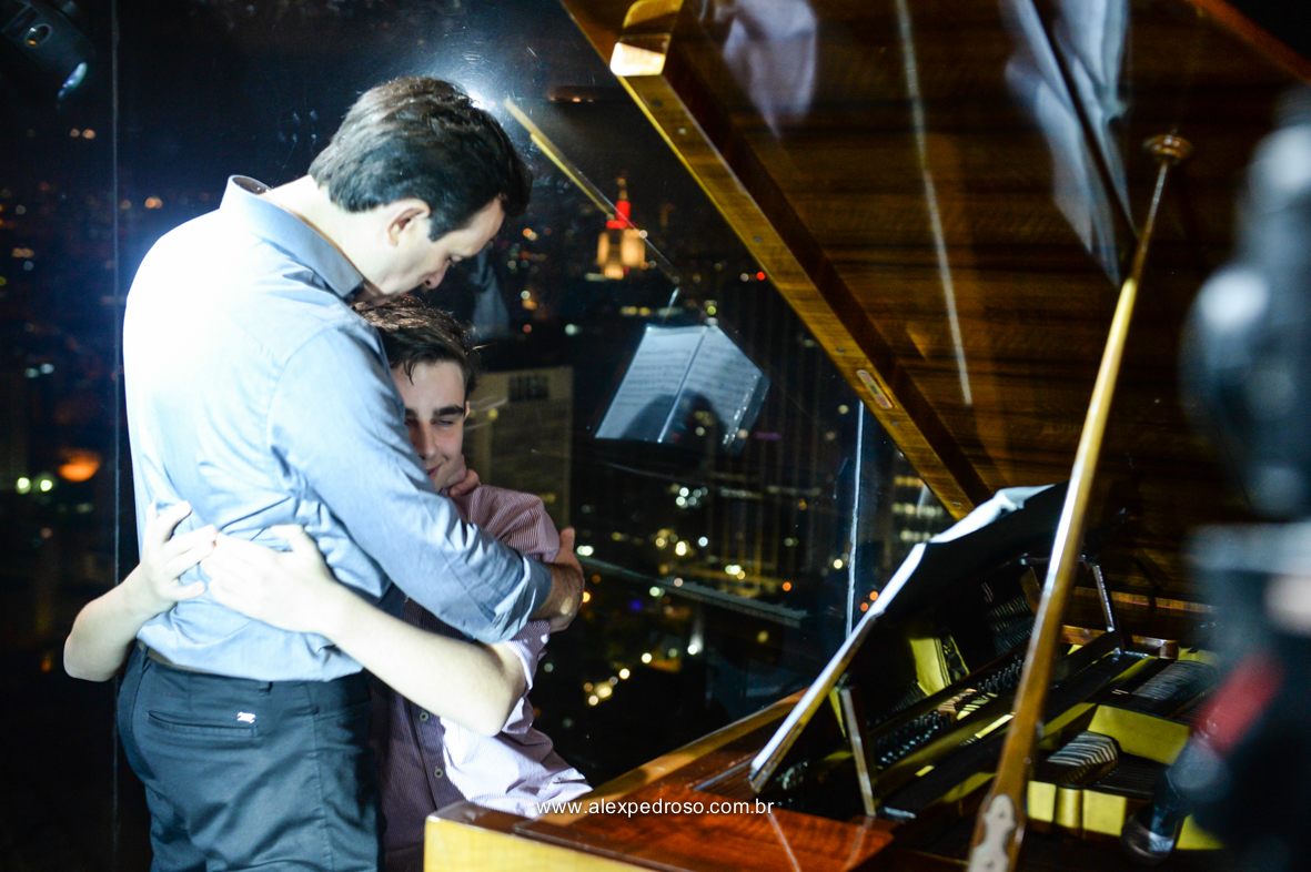 filho abraçando o pai ao lado  piano no restaurante Terraço Italia no predio circulo italiana com a vista de sao paulo a noite de fundo 