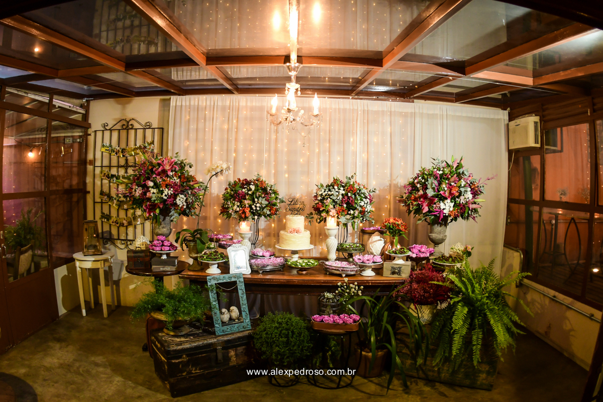 mesa do bolo de casamento decorada com flores e doces finos com um lustre ao centro no espaço flores na varanda 