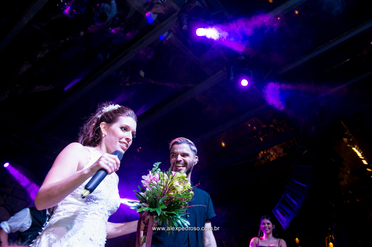 noiva no palco com o buque na mao e microfone chamando as amigas solteiras para vir tenta a sorte e pegar o buque
