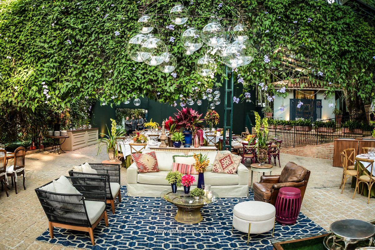 laud montado com sofa e cadeiras decorativas com tapete e mesa de centro em vidro com flores em cima e iluminação com veles no teto