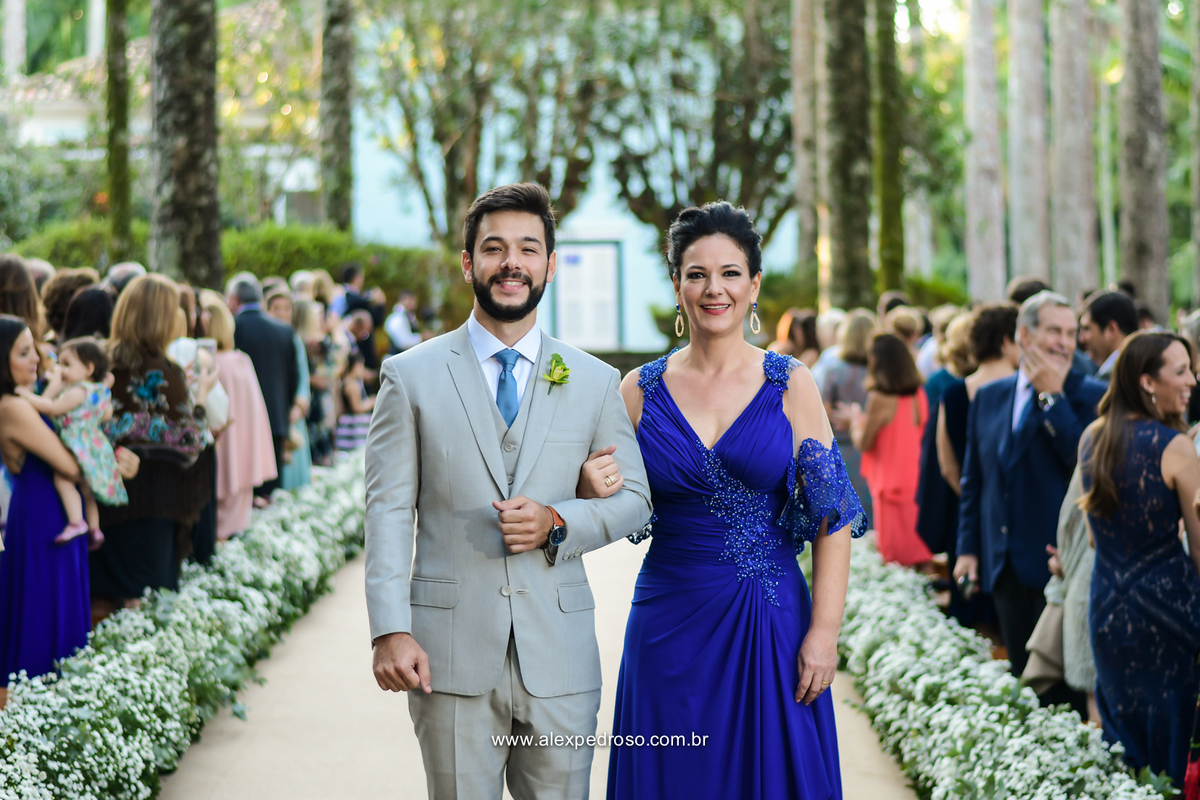 entrada do noivo com a mae no corredor todo decorado com flores e um tapete de palha com os convidados olhando para ele