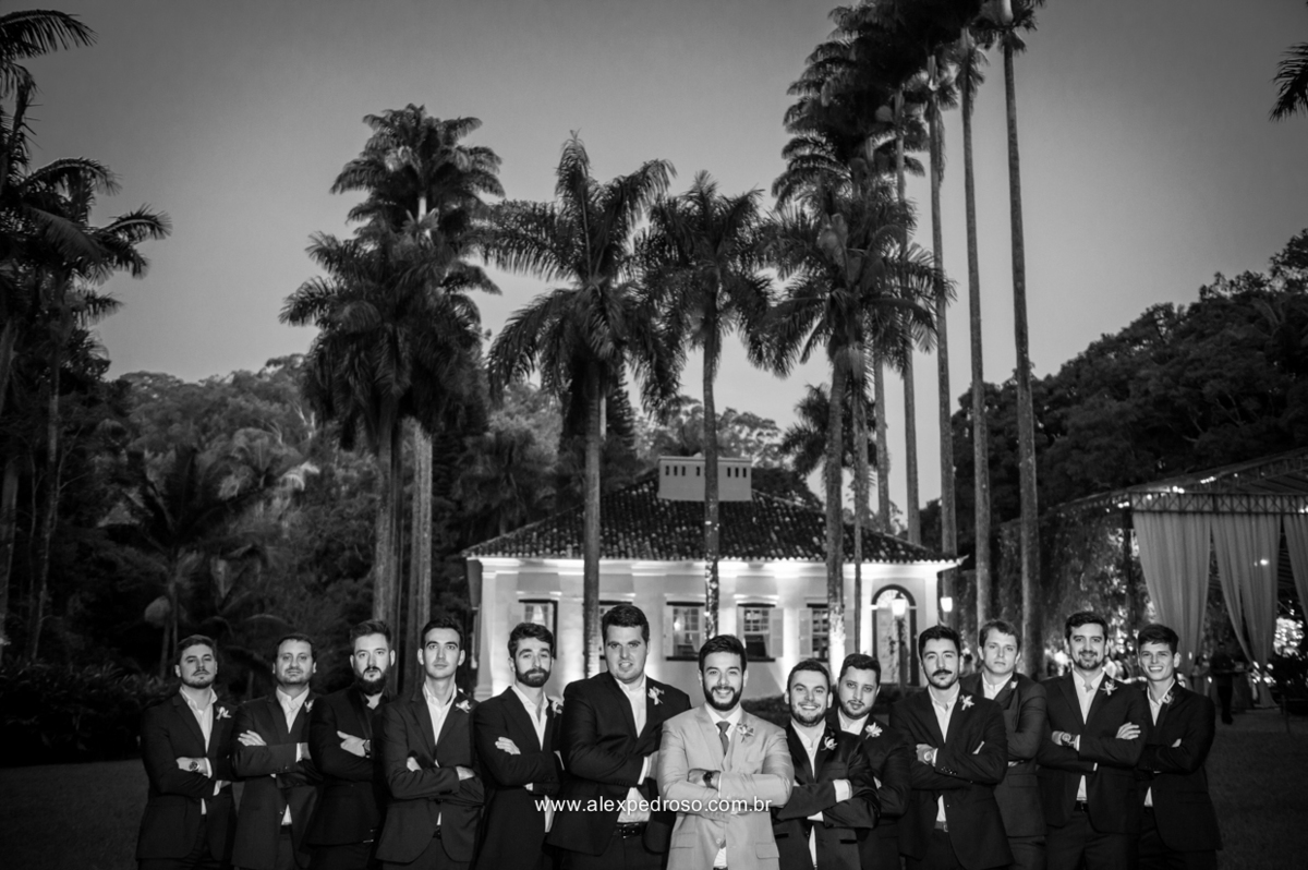 noivo se  junto com todos os padrinhos no gramado com o casarão da fazenda vila rica ao fundo foto feita em preto em branco com todos de braco cruzados