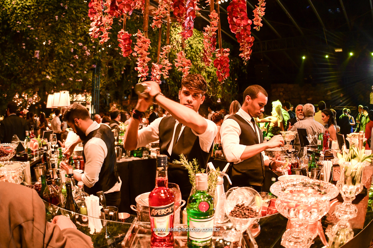 barman fazendo bebidas e drinks com os convidas ao lado e a pista de fundo