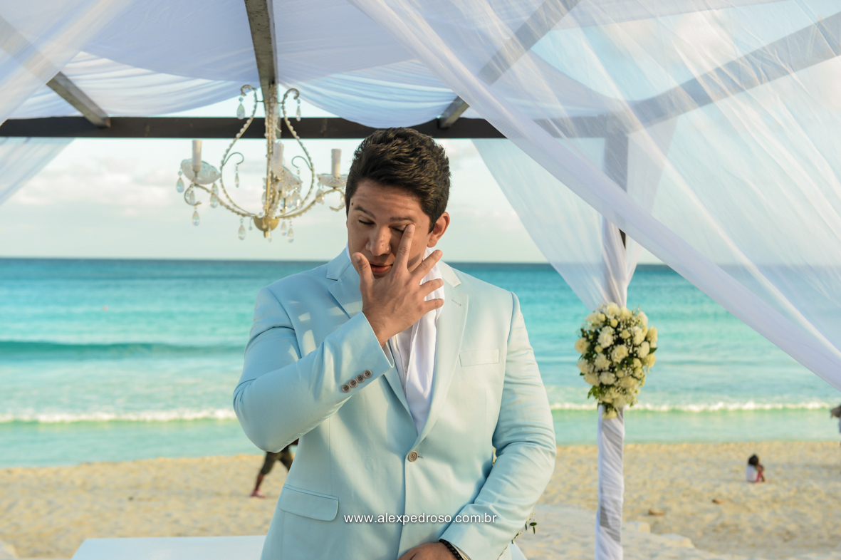noivo vestido azul claro um terno do Ricardo Almeida chorando no momento que viu sua noiva vestida de branco e com o mar a suas costa fazendo fundo no Mandala Beach Club
