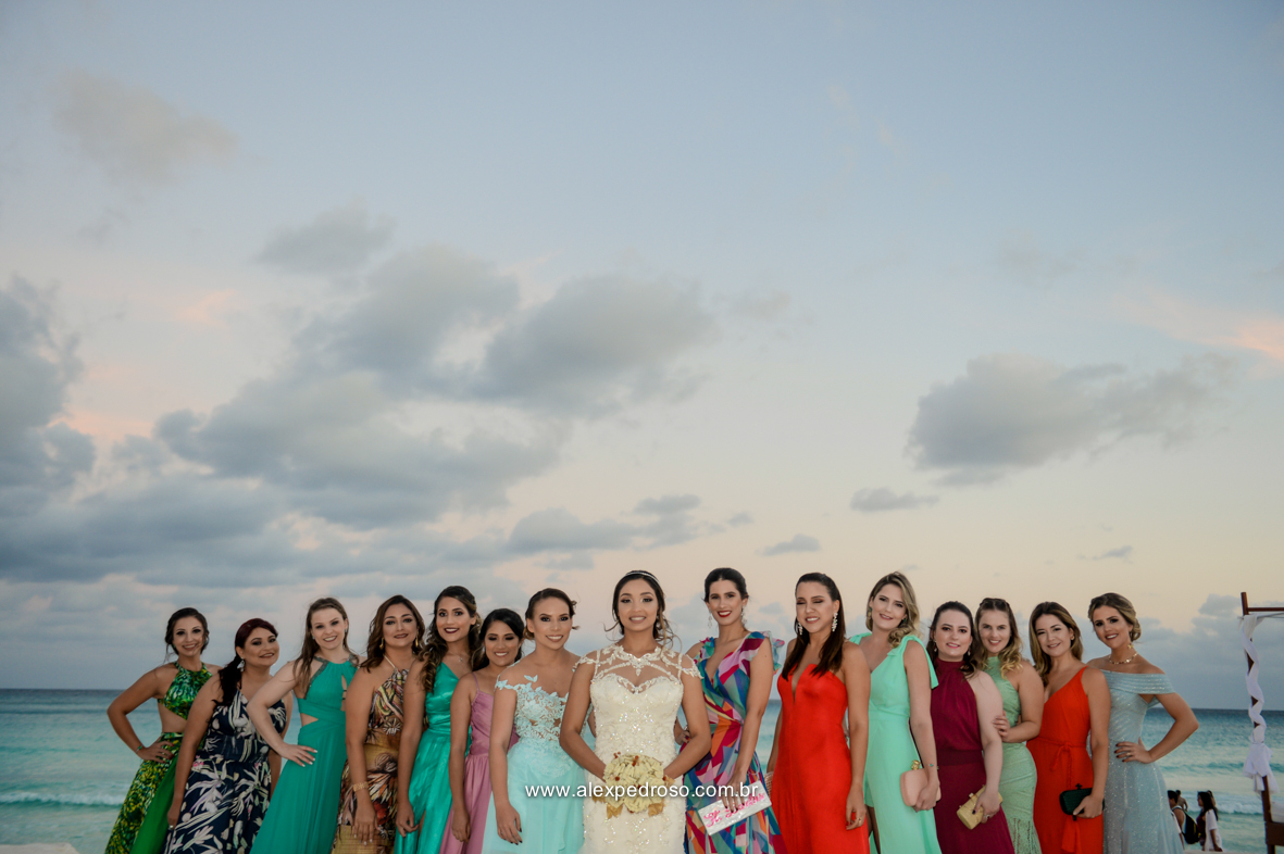 noiva no centro e suas madrinhas ao lado com o mar e o ceu azul ao fundo 
