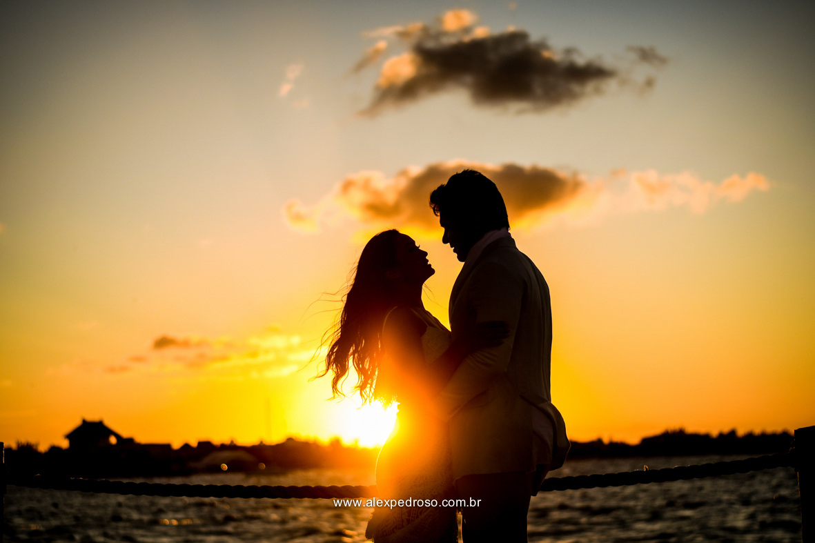 noiva vestindo brando com um vestido mais solto e noivo vestindo terno Azul Clora do Ricardo almeida  bem juntos com o por do sol ao fundo o mar aparecendo no deck no mar do caribe no mexico 