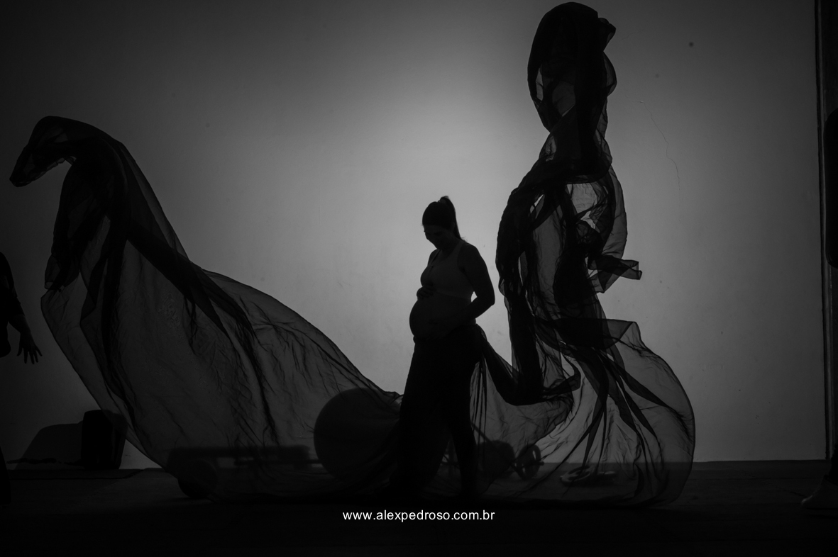 Foto de gestante em uma academia com tecidos vermelhos jogados pra cima, formando uma borboleta com um top laranja, feito em silhueta em preto e branco