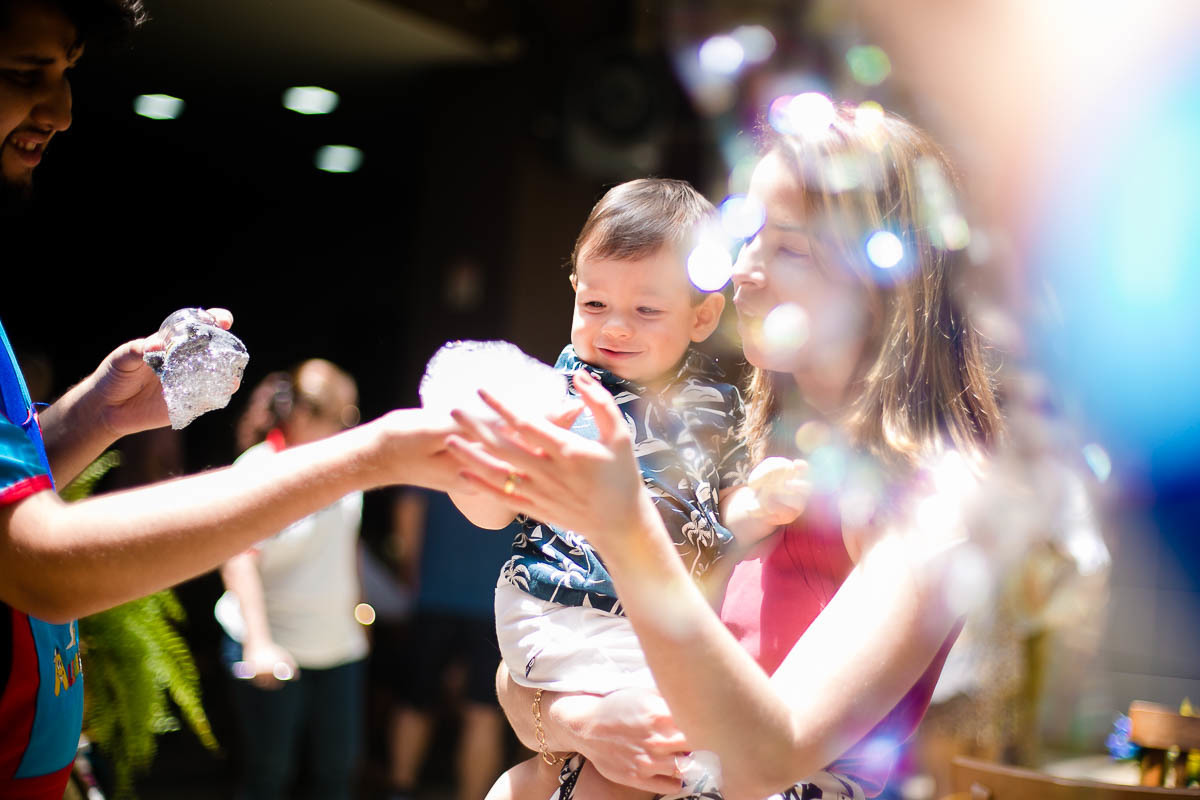 fotografa-jaqueline-porto-festa-tema-praia-casa-de-festas-pitanga-pitangueira-em-botafogo-aniversariante-brincando-com-de-bolinha-de-sabao-no-colo-da-mae