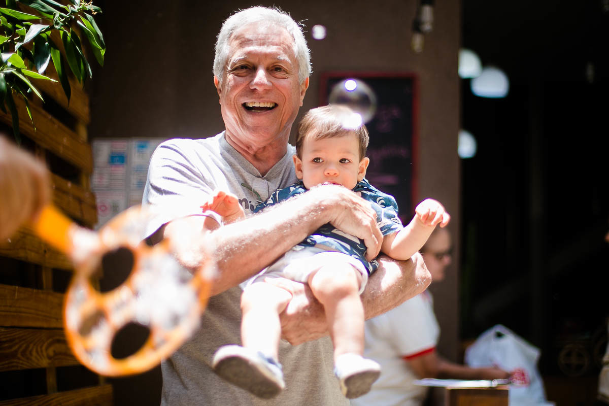 festa-tema-praia-casa-de-festas-pitanga-pitangueira-em-botafogo-aniversariante-brincando-com-de-bolinha-de-sabao-no-colo-do-avo-materno-jaqueline-porto-fotografia