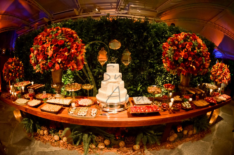 Casamento Zéfiro Niterói, mesa de doces e bolo com flores laranja e vermelho, paisagismo sob a mesa, muro inglês e espelhos.