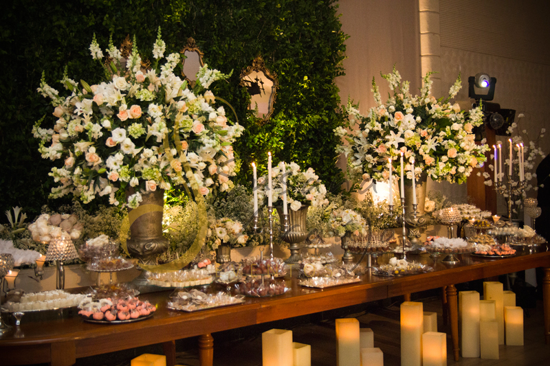 Casamento Rio Cricket Niterói, mesa de doces e bolo com flores e arranjos de flores brancas, e mobiliário de madeira.  Velas, castiçais, muro inglês e espelhos.
