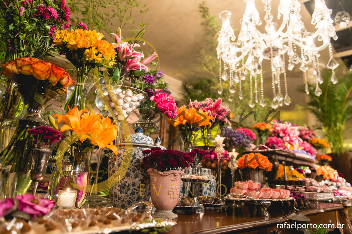 mesa de doces e bolo com flores e arranjos de flores rosa, laranja, brancas, e mobiliário de madeira. 