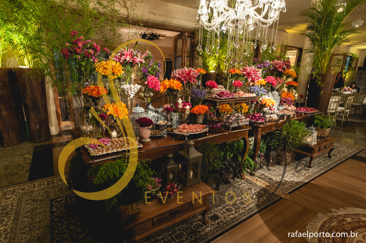 mesa de doces e bolo com flores e arranjos de flores rosa, laranja, brancas, e mobiliário de madeira. 