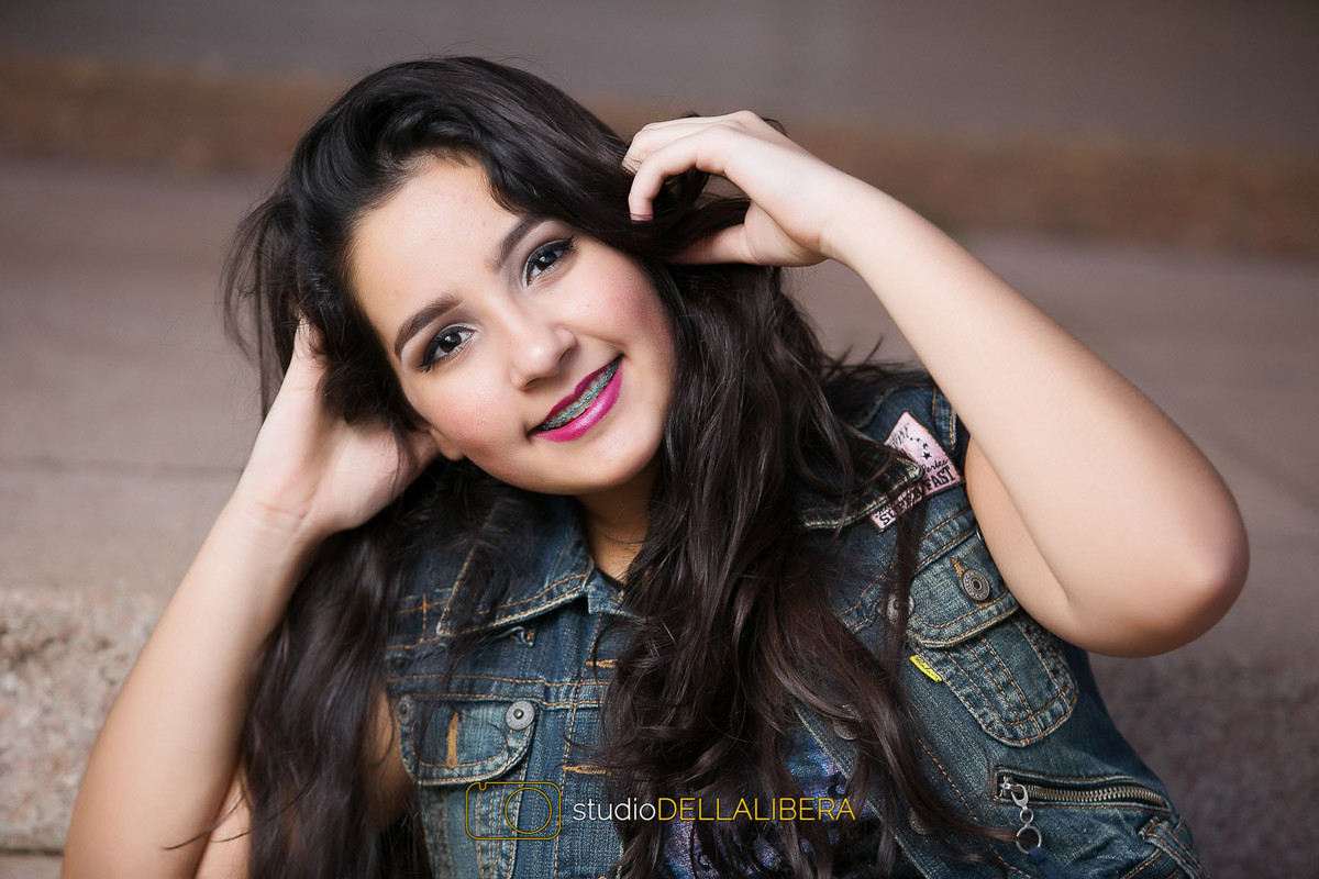 Laura de colete jeans sentada com as mãos na cabeça modelando na escada da Esalq na sessão de foto em família