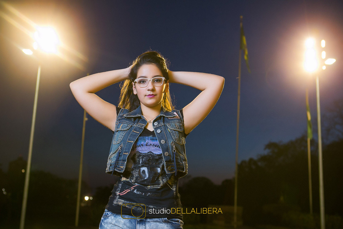 Laura modelando em Piracicaba SP com bandeira do brasil ao fundo e mãos na cabeça de oculos e jaqueta jeans